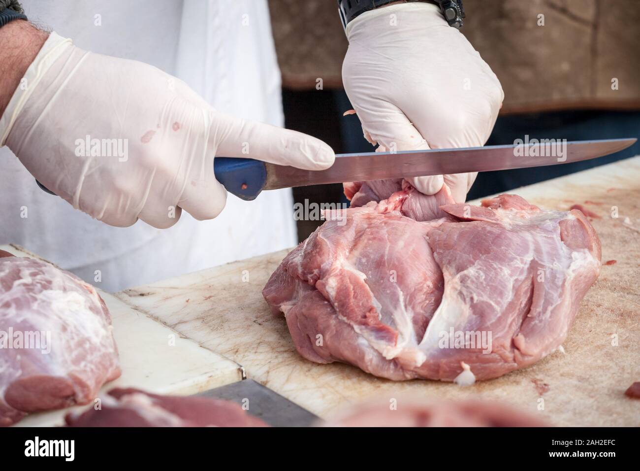 Le mani di un macellaio professionale di taglio di un pezzo di carne di maiale cruda con un coltello lungo, su un listone bianco, in corrispondenza di una macelleria rurale della Serbia. La carne di maiale è uno Foto Stock