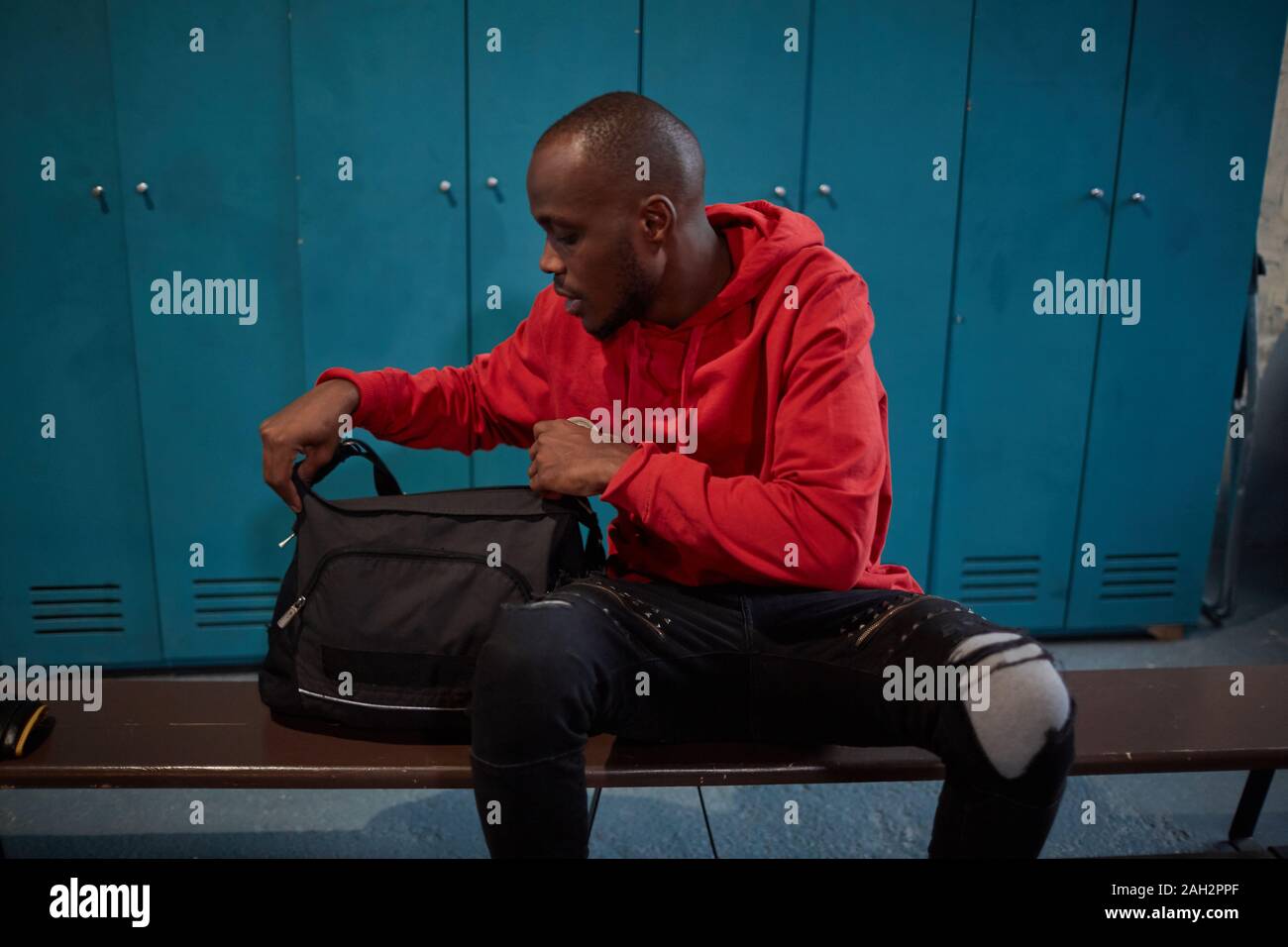 I giovani africani uomo seduto su un banco di lavoro e di apertura della sua borsa egli prepara per la formazione sportiva in spogliatoio Foto Stock