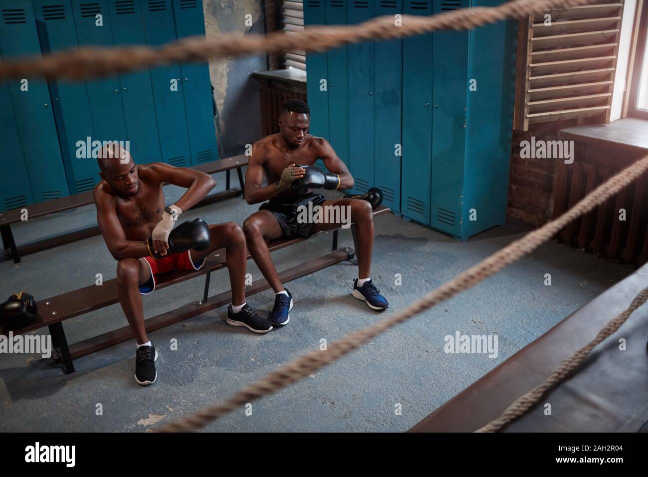 Due pugili africani seduta sul banco e indossando guanti di inscatolamento e preparazione per la formazione sportiva Foto Stock
