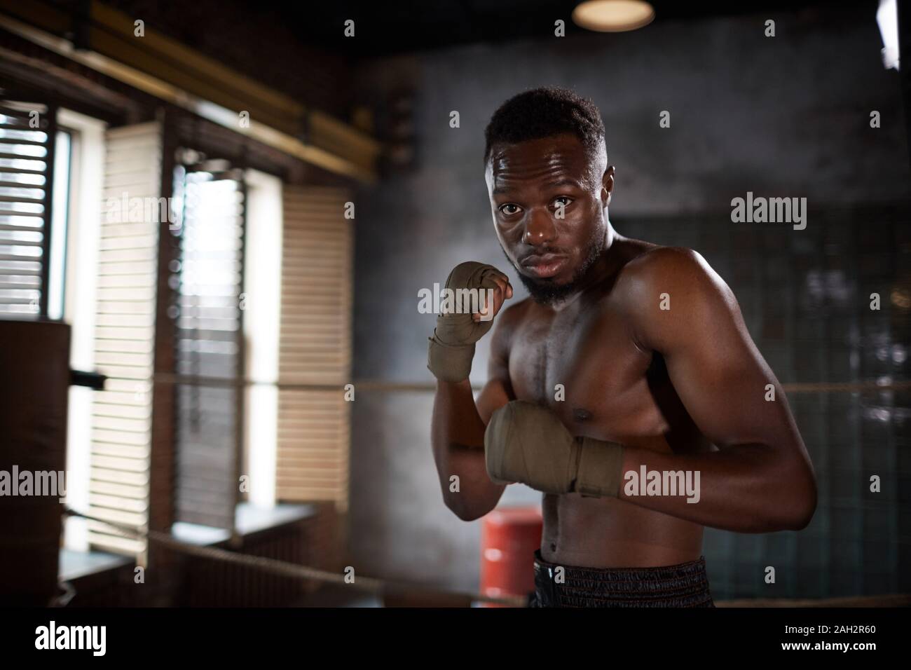 Ritratto di giovane africano muscolare di uomo in piedi e in posa in telecamera durante gli allenamenti in palestra Foto Stock
