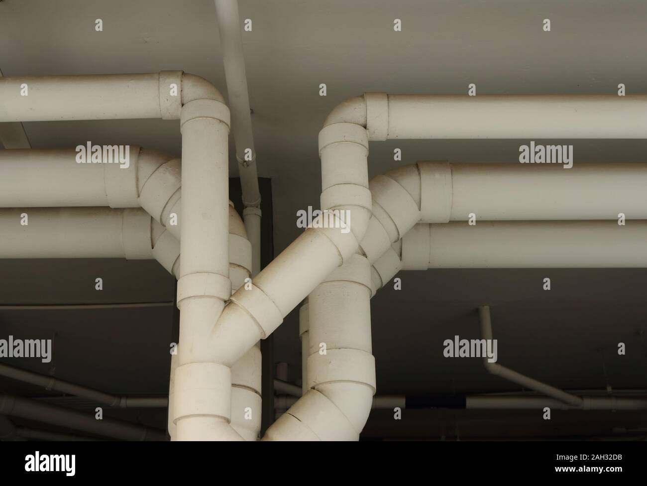 Closeup fila di plastica grandi tubi di acqua verniciato con colore bianco eseguire sotto il soffitto di un edificio, il fuoco selettivo Foto Stock