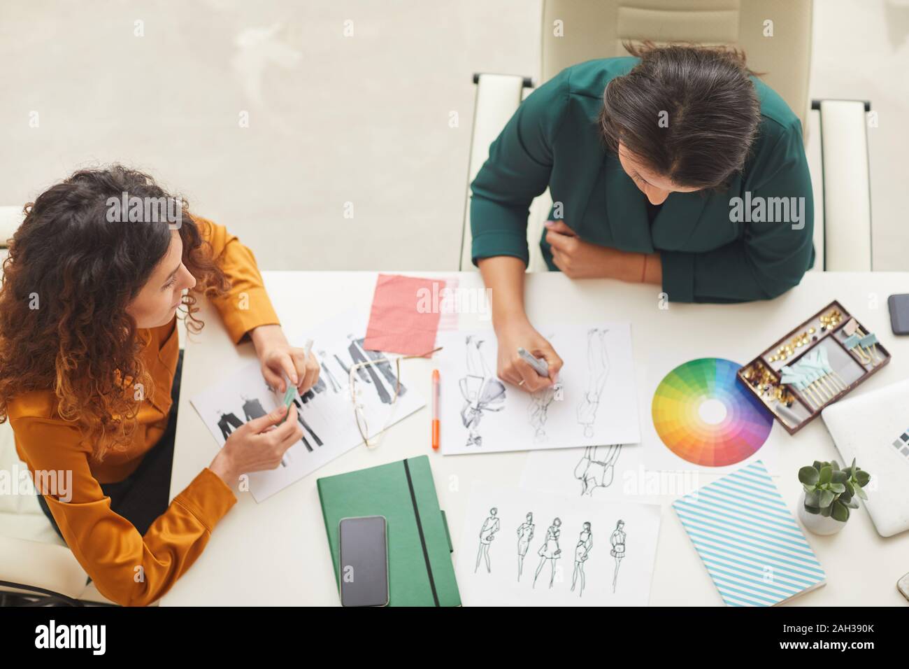 Due eleganti giovani donne creazione di fashion design schizzi seduti insieme a Office tabella, parte superiore orizzontale vew shot Foto Stock