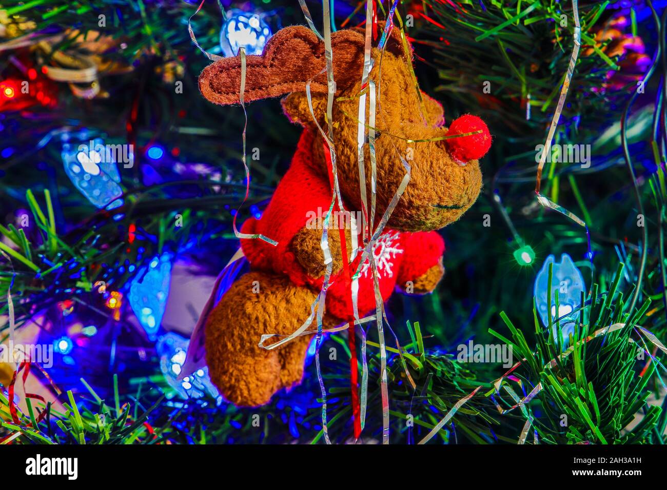 Morbide renne giocattolo pendente da albero di Natale visto con tinsel e luci. Prese a Kings Lynn, Norfolk, Regno Unito il 23 Dic 2019. Foto Stock