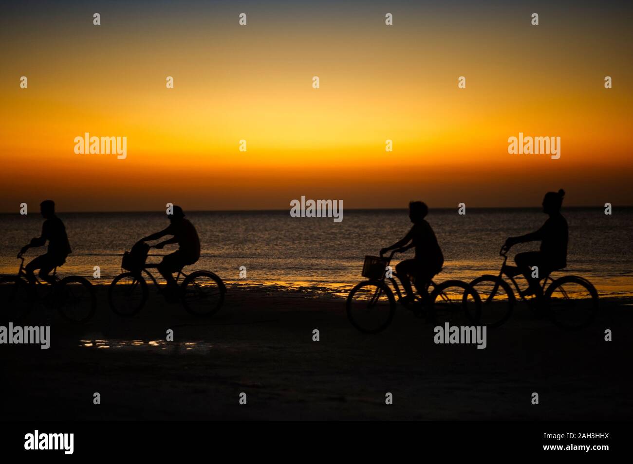 Una corsa in bicicletta sull'isola di Holbox spiaggia tramonto in Messico. Persone in bicicletta sulla spiaggia caraibica al tramonto. Foto Stock