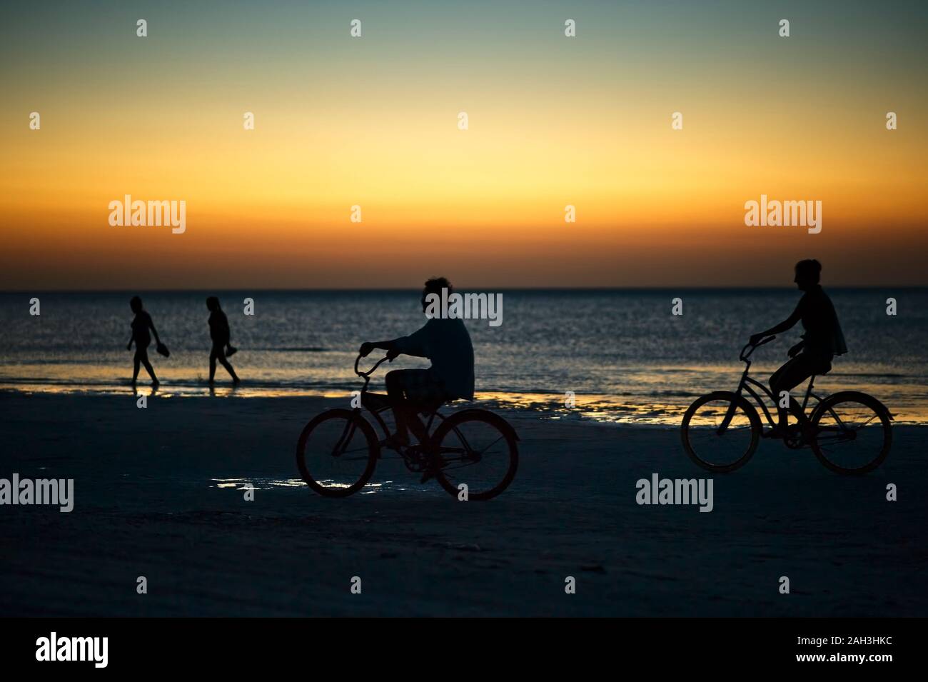 Una corsa in bicicletta sull'isola di Holbox spiaggia tramonto in Messico. Persone in bicicletta sulla spiaggia caraibica al tramonto. Foto Stock
