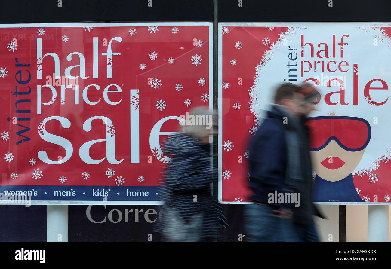 Gli acquirenti di Natale a piedi passato un segno di vendita nella finestra di Debenhams su Winchester High Street, negozi come prepararsi per il boxing day vendite. Foto Stock