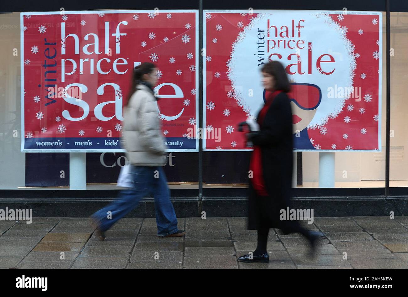 Gli acquirenti di Natale a piedi passato un segno di vendita nella finestra di Debenhams su Winchester High Street, negozi come prepararsi per il boxing day vendite. Foto Stock