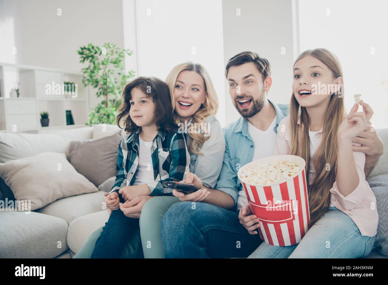 Foto della grande famiglia di quattro membri trascorrere il tempo libero guardando la tv mostra sit lettino mangiare popcorn salato Foto Stock