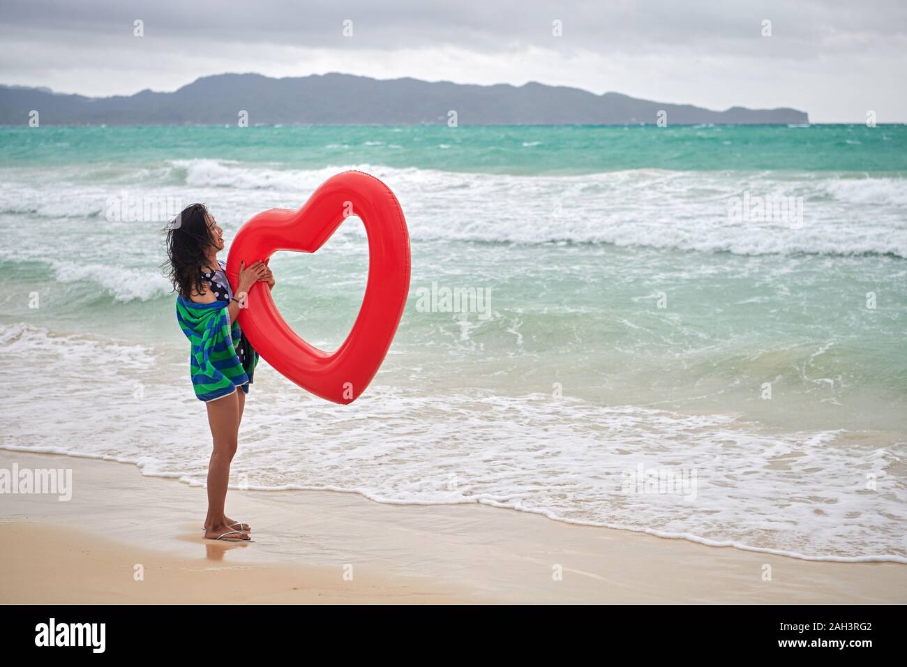 Il Boracay, Aklan Provincia, Filippine - 3 Dicembre 2019: una giovane bella donna asiatica avvolto in un telo da spiaggia è in possesso di un rosso a forma di cuore ad anello ad aria Foto Stock