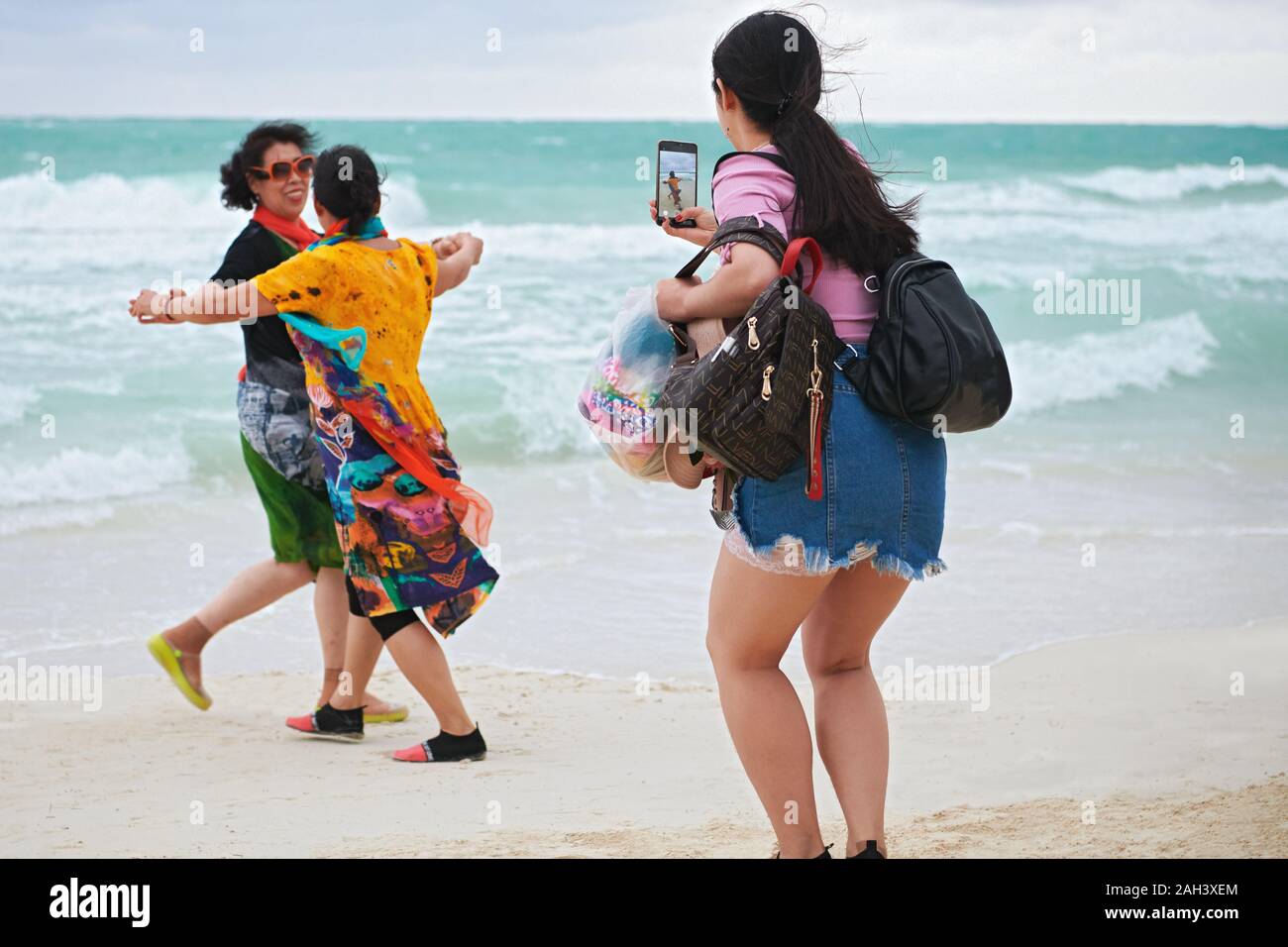 Il Boracay, Aklan Provincia, Filippine - 3 Dicembre 2019: una donna fare una foto da due donne asiatiche in abiti colorati balli presso la spiaggia di sabbia bianca Foto Stock