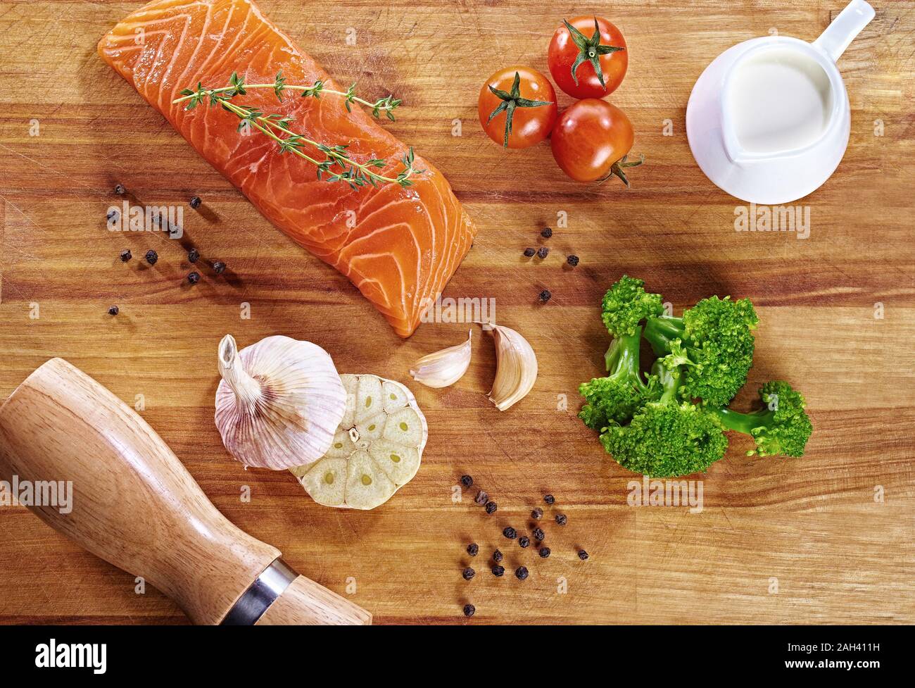 Set di cibo sano anticancro su tavolo di legno. Salmone rosso, broccoli, aglio, latte, pepe e pomodori sparsi intorno ad un tavolo. Pasto sano Foto Stock