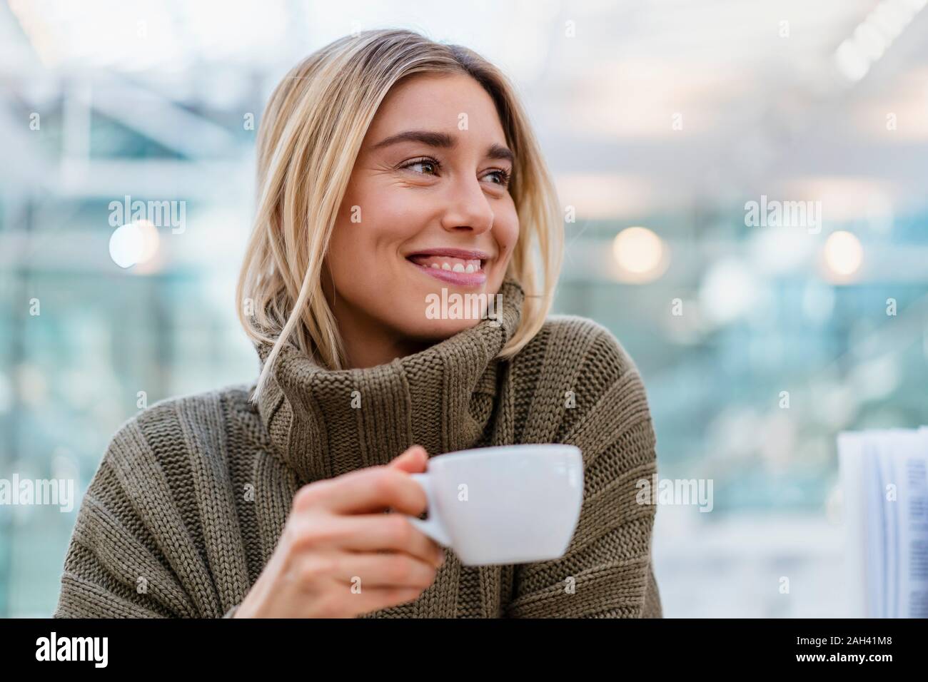 Ritratto di un sorridente giovane donna azienda tazza di caffè guardando lontano Foto Stock