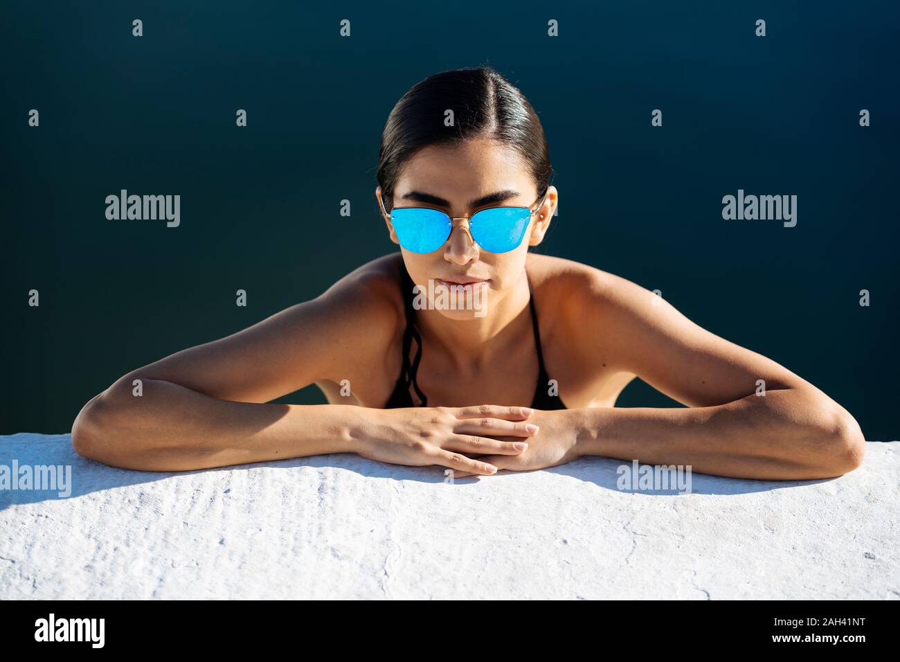 Ritratto di giovane donna che indossa gli occhiali da sole e bikini appoggiata sulla parete quay Foto Stock