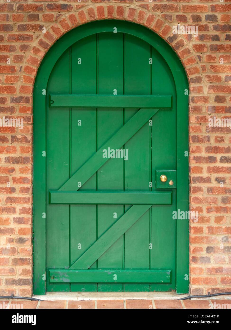 Chiuso dipinte di verde porta di legno in apertura ad arco in mattoni rossi a parete, Barnsdale Gardens, Rutland, England, Regno Unito Foto Stock