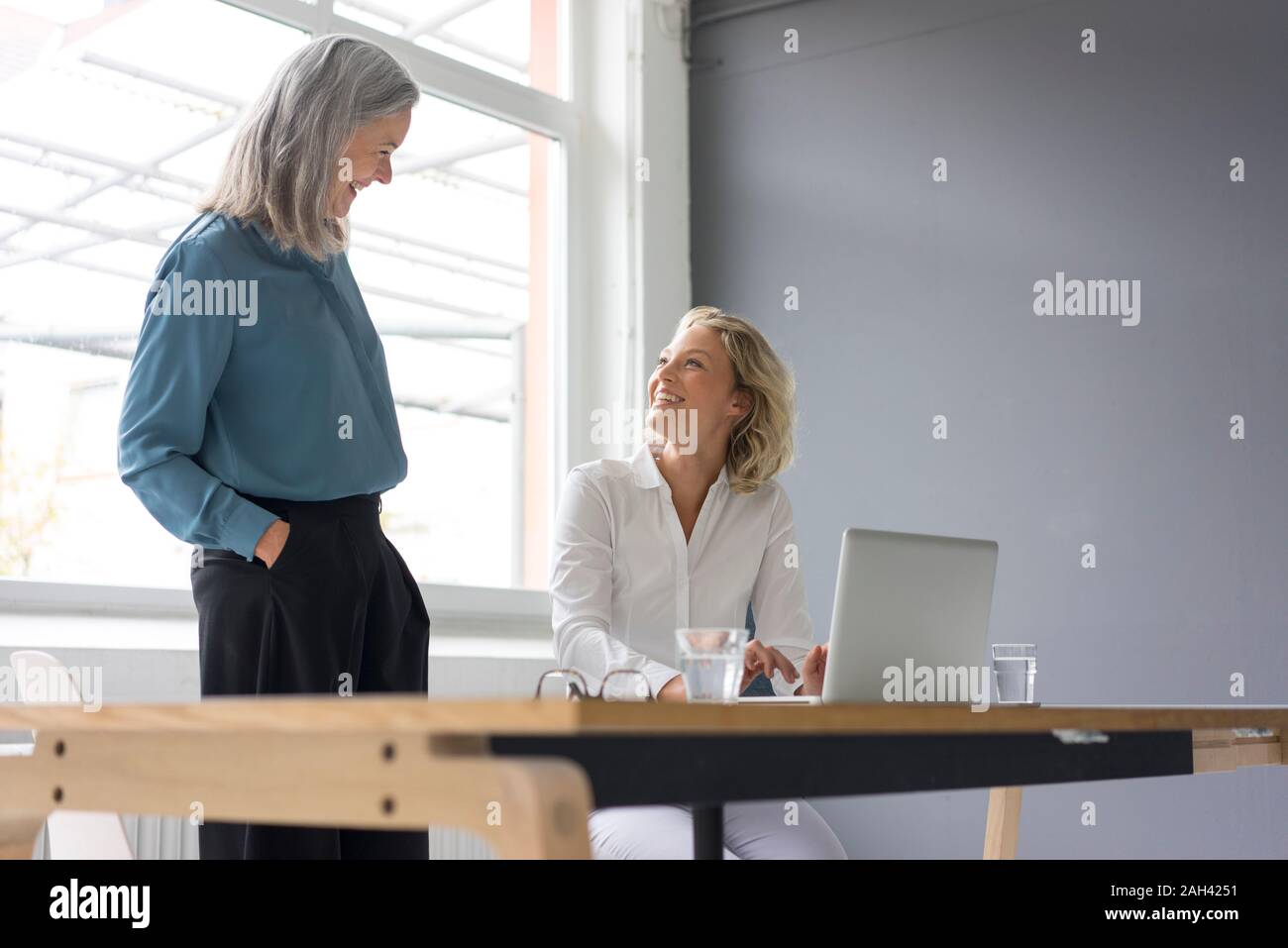 Due imprenditrici sorridente ad ogni altra alla scrivania in ufficio insieme Foto Stock