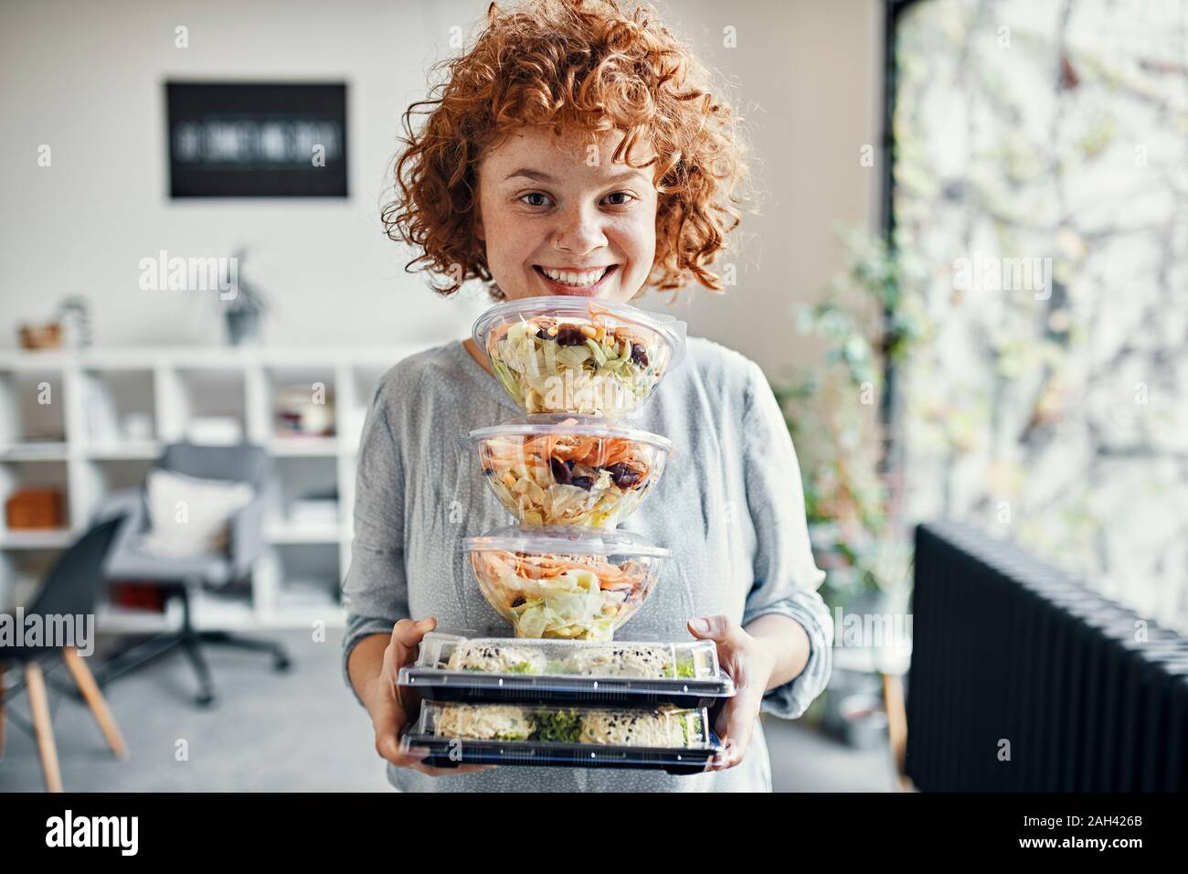 Ritratto di sorridere imprenditrice stack di contenimento di cibo da asporto in office Foto Stock