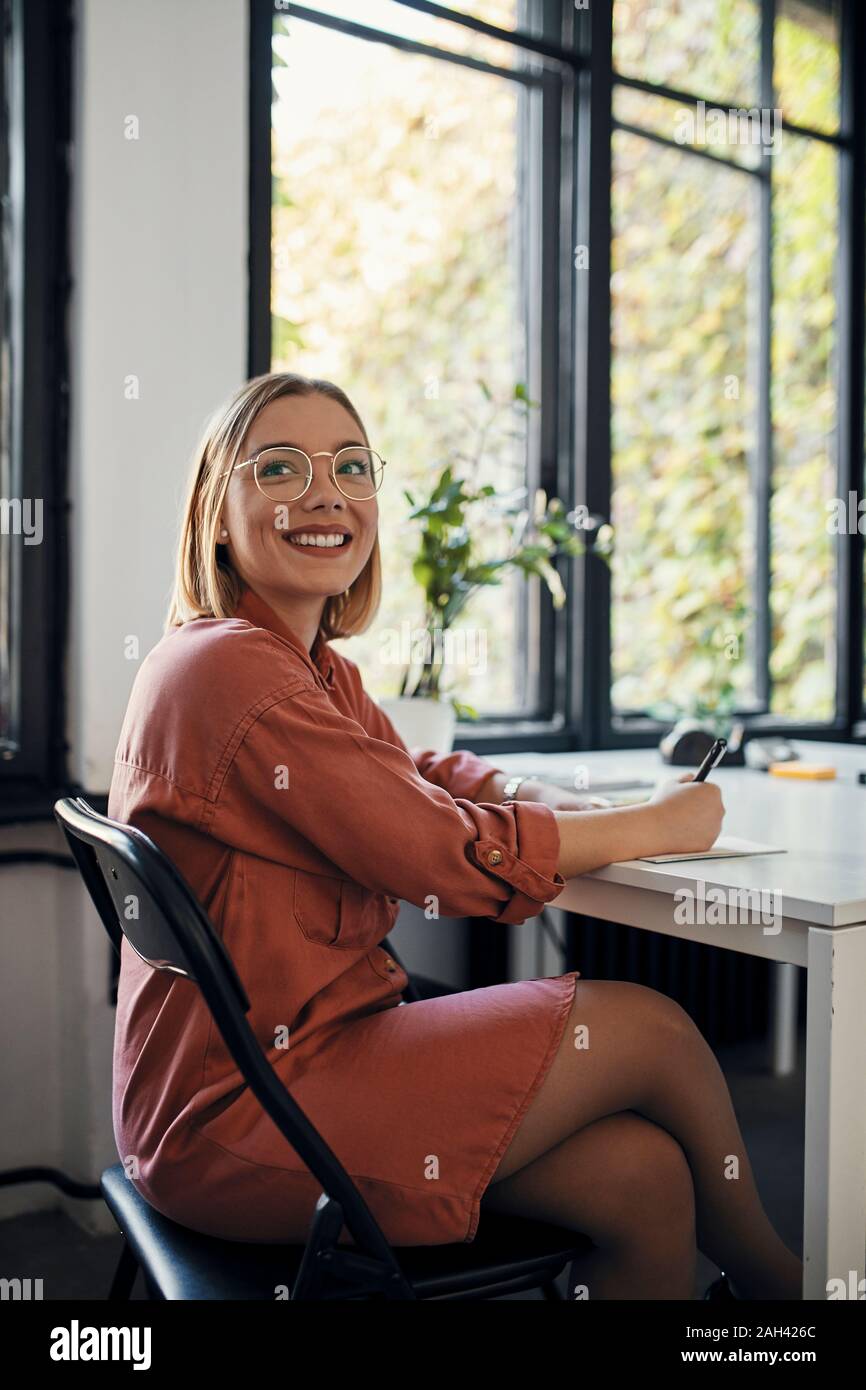 Ritratto di sorridere imprenditrice prendendo appunti alla scrivania in ufficio Foto Stock