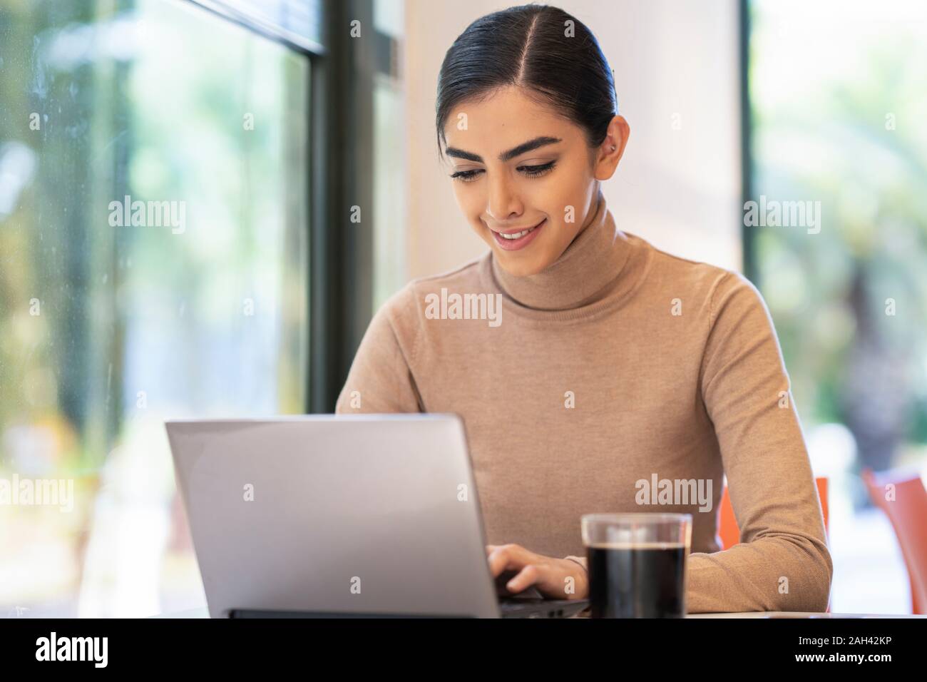 Sorridente giovane donna utilizzando laptop in un cafe Foto Stock