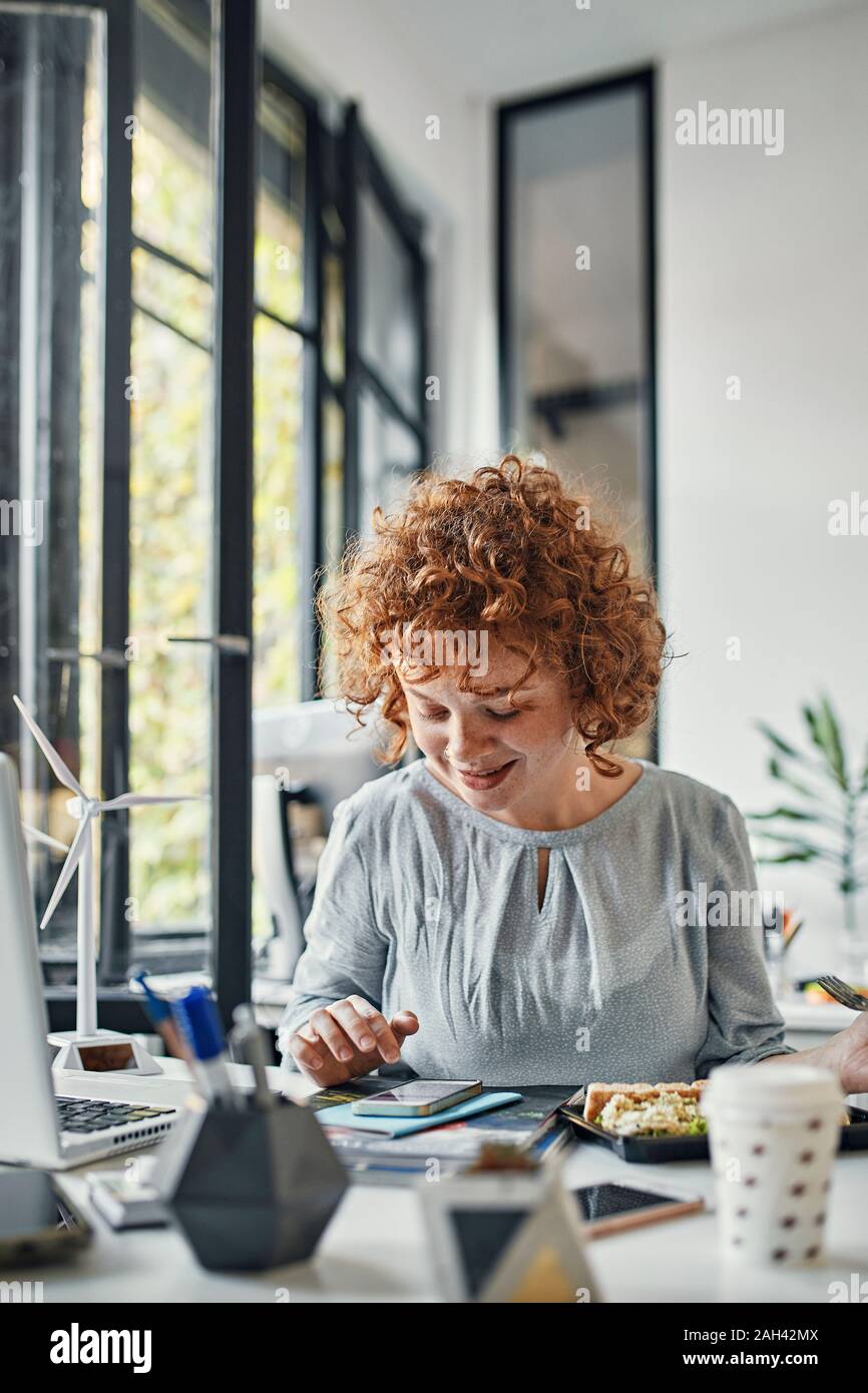Imprenditrice utilizza lo smartphone durante la pausa pranzo in ufficio Foto Stock