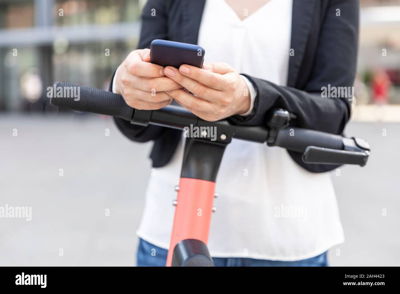 Donna che si trova in città, Berlino, Germania, con e-scooter che utilizza uno smartphone Foto Stock