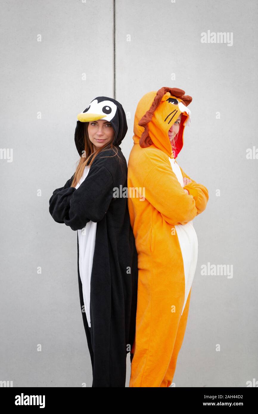 Due donne in penguin e lion costume, di schiena nella parte anteriore della parete di cemento Foto Stock