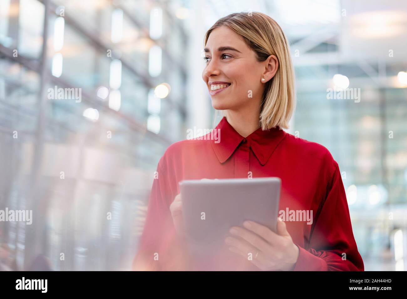 Sorridente giovane imprenditrice indossando maglietta rossa utilizzando tablet Foto Stock