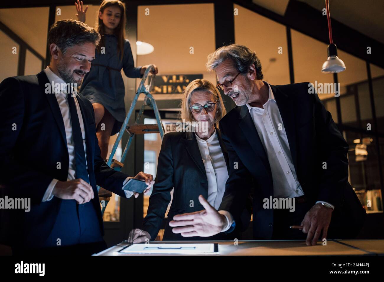 La gente di affari discutendo a shining tablet in ufficio con la ragazza sulla scala in piedi oltre Foto Stock