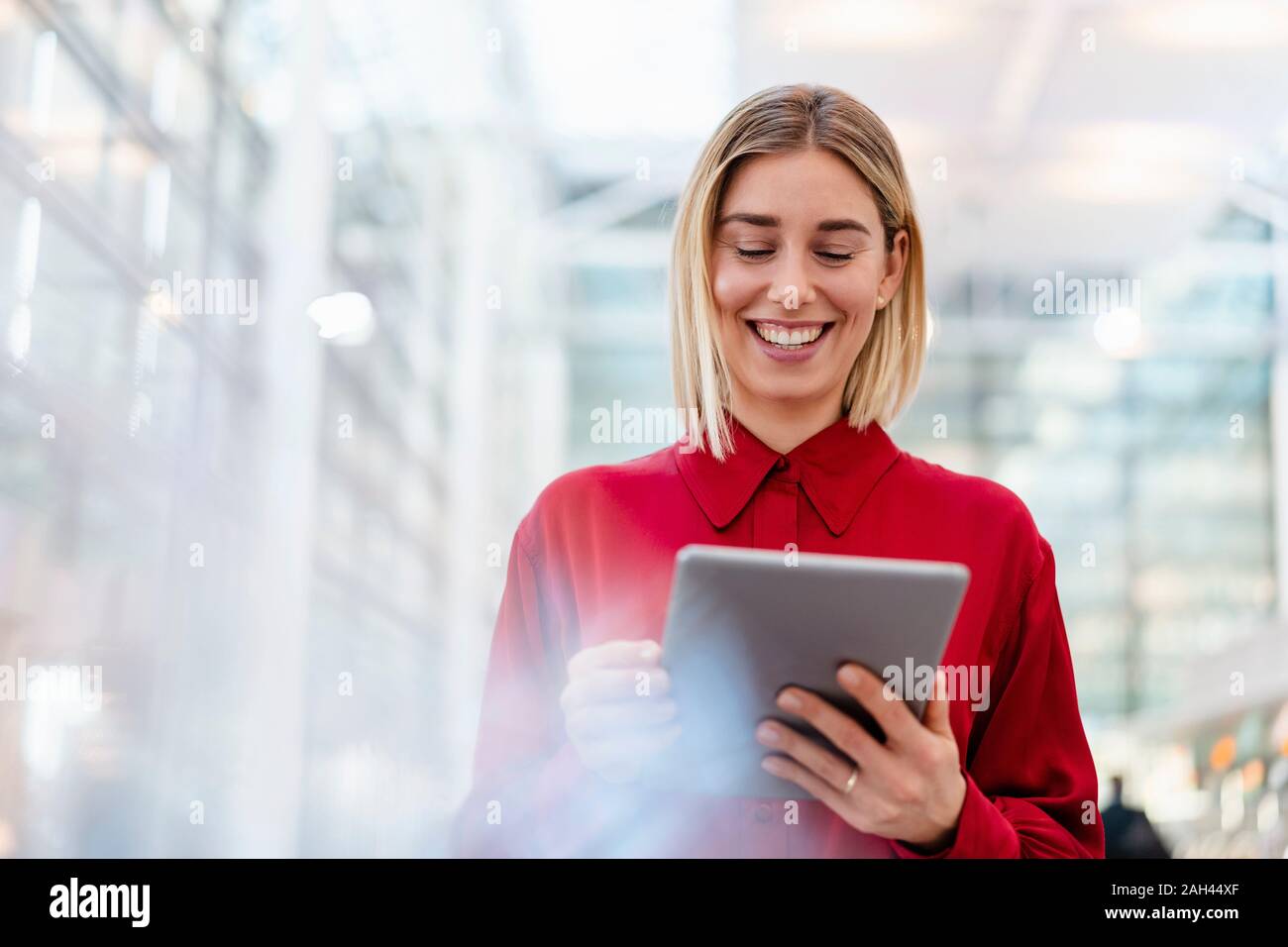 Felice giovane imprenditrice indossando maglietta rossa utilizzando tablet Foto Stock