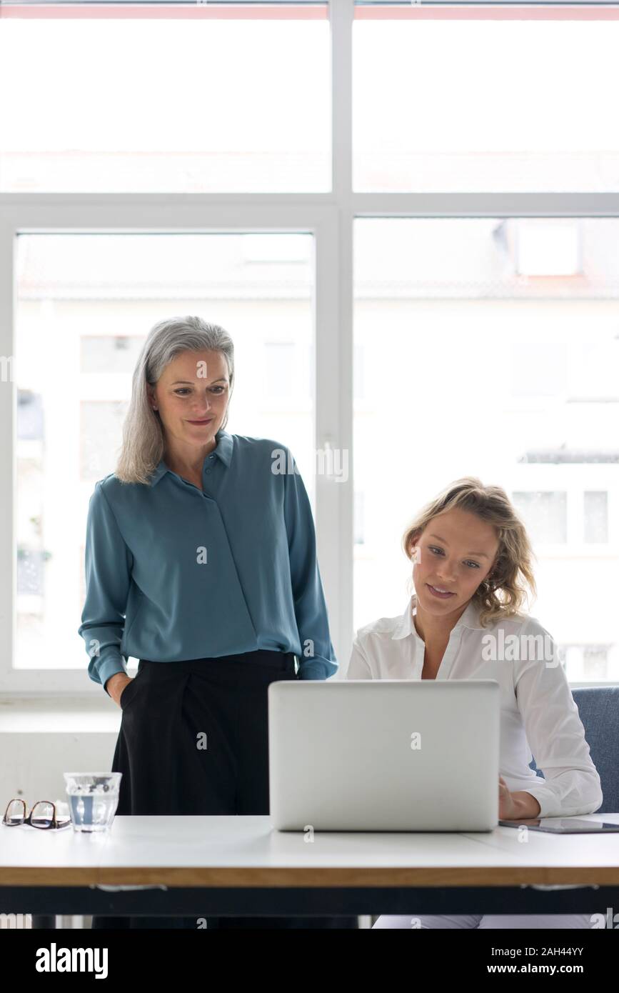 Due imprenditrici utilizzando laptop alla scrivania in ufficio insieme Foto Stock