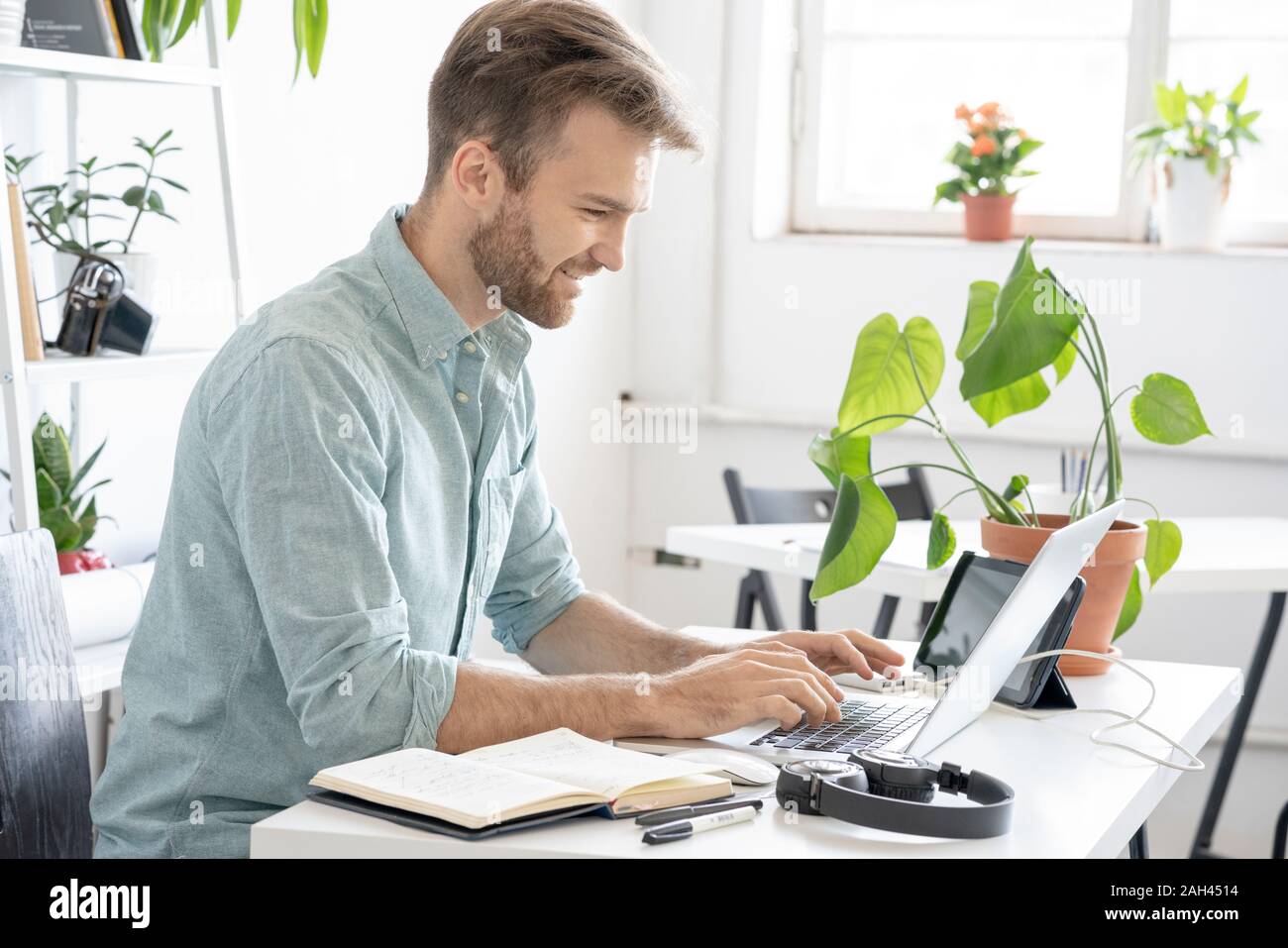 Uomo sorridente con notebook alla scrivania in ufficio Foto Stock