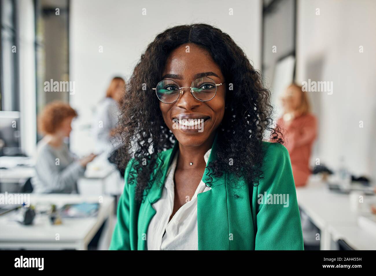 Ritratto di una imprenditrice sorridente in ufficio con i colleghi in background Foto Stock