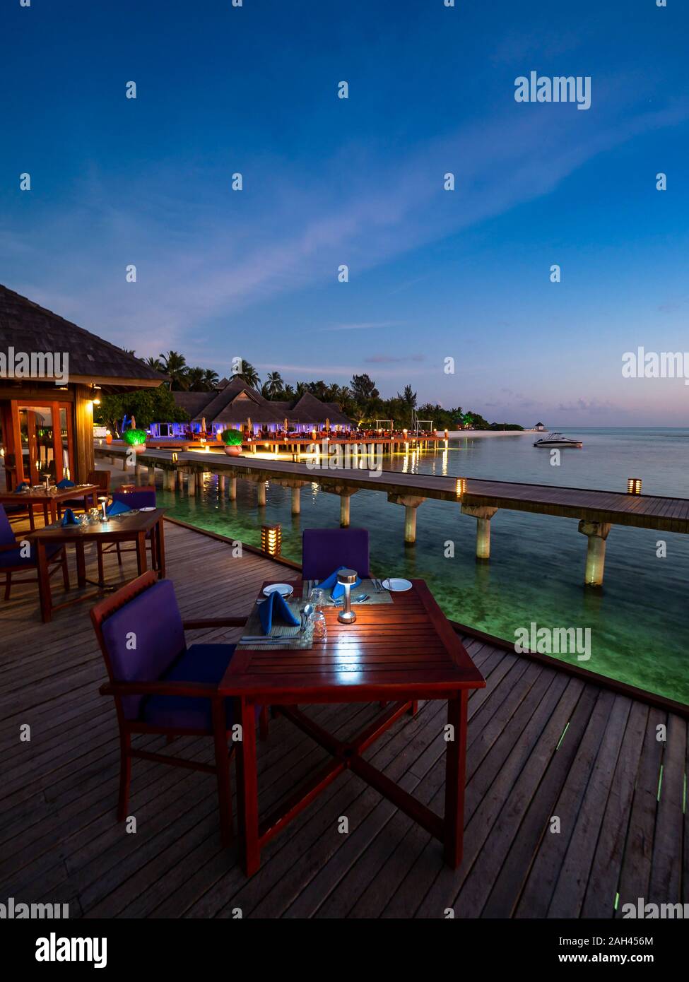 Maldive, tavoli da pranzo del ristorante costiero al tramonto con il molo in background Foto Stock