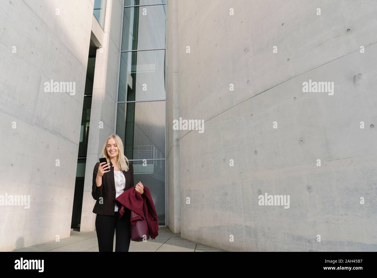 La bionda imprenditrice utilizza lo smartphone in background e moderni edifici Foto Stock