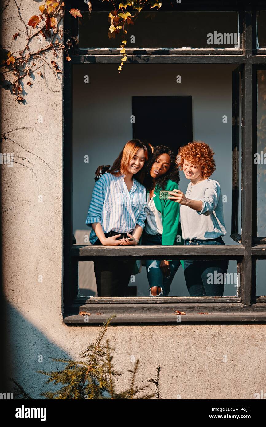 Tre imprenditrici in piedi presso la finestra di un edificio per uffici di prendere una selfie Foto Stock