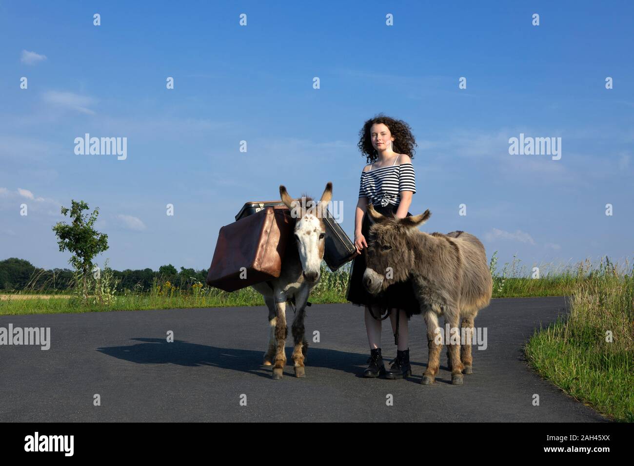 Giovane donna in piedi sulla strada di campagna con gli asini che trasportano bagagli Foto Stock