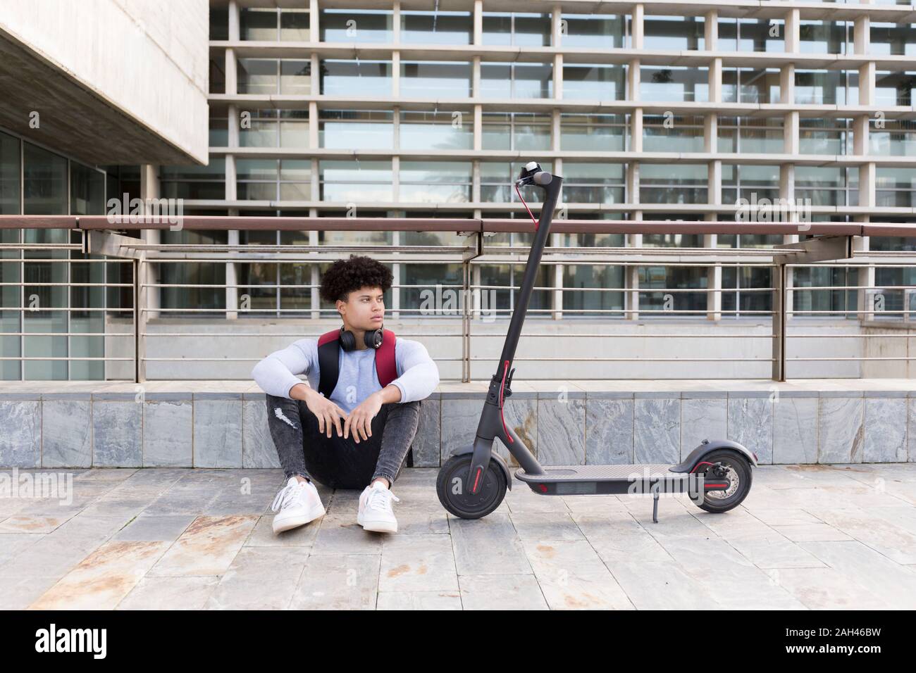 Giovane uomo con e-scooter seduti nella città Foto Stock