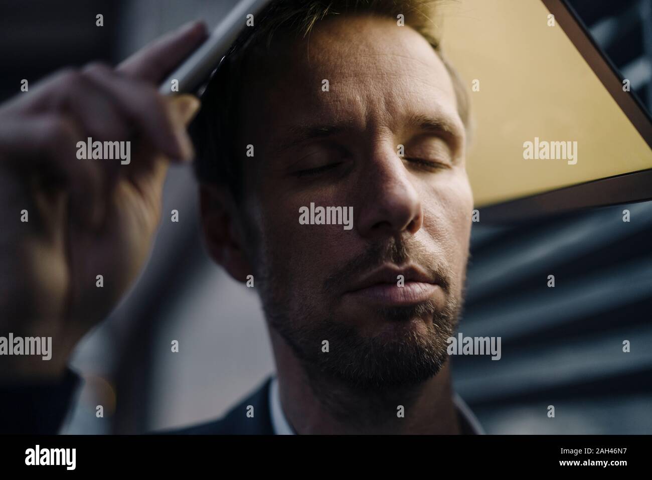 Imprenditore con gli occhi chiusi tenendo accesa laptop sopra la sua testa Foto Stock