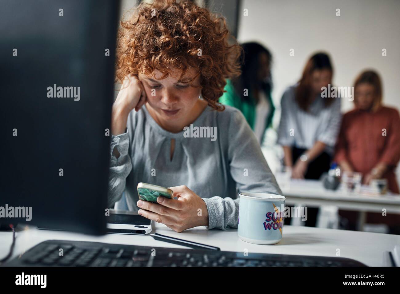 Imprenditrice utilizza lo smartphone alla scrivania in ufficio Foto Stock