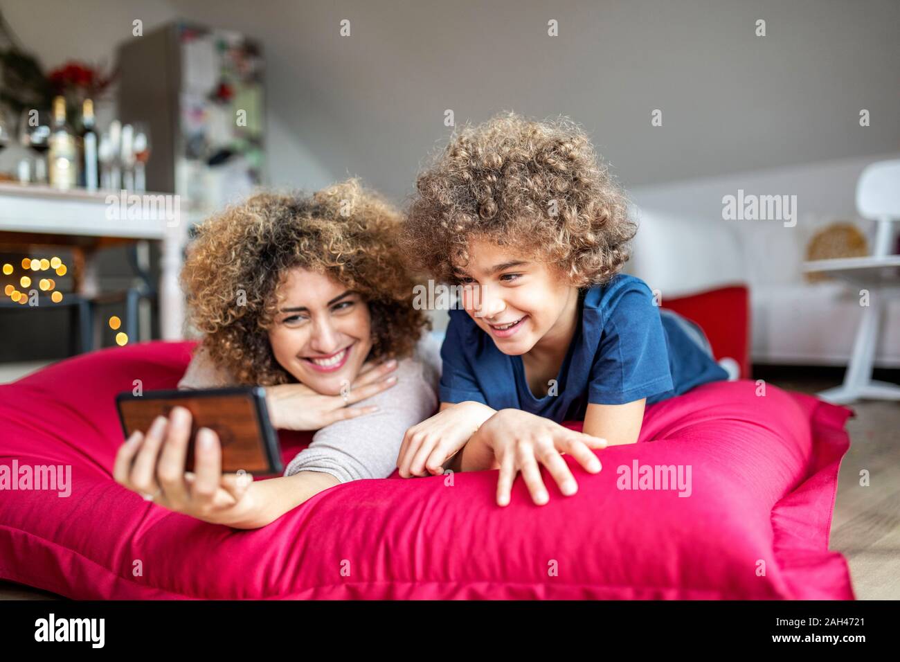 Madre e figlio guardando un video sullo smartphone, giacente sul cuscino di grandi dimensioni Foto Stock