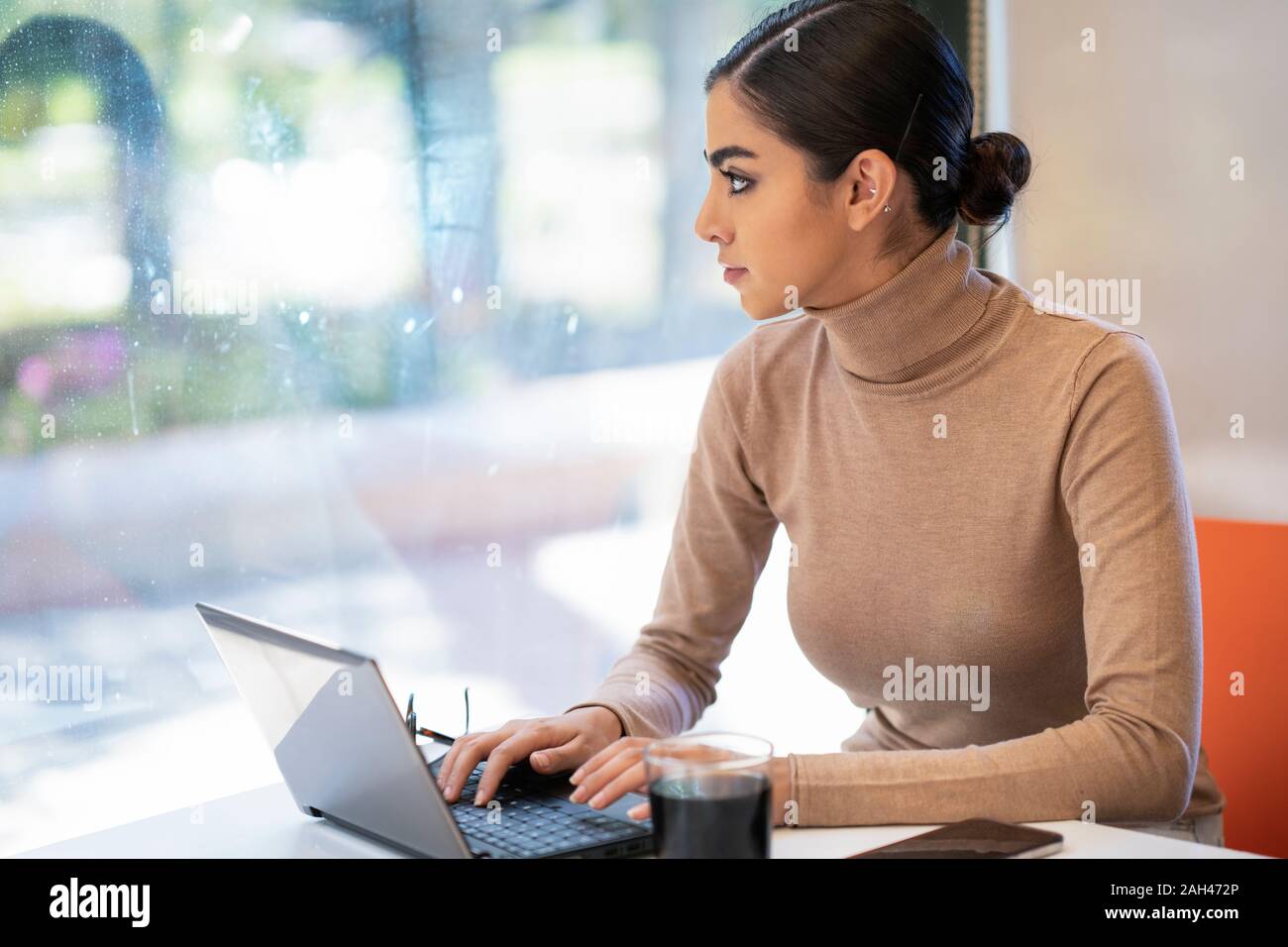 Giovane donna utilizzando laptop in un cafe e guardando fuori della finestra Foto Stock
