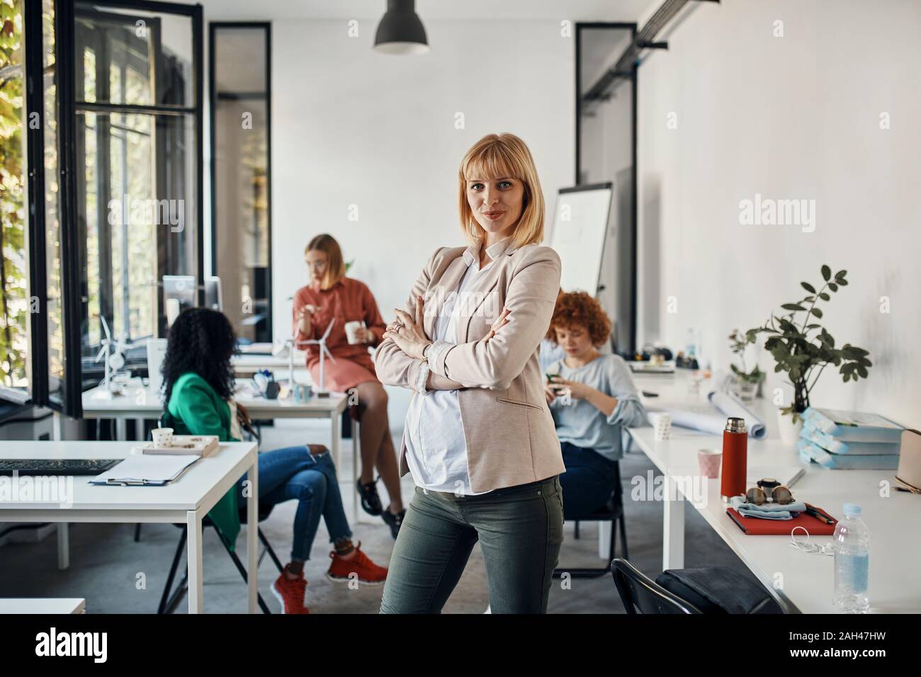 Ritratto di fiducioso incinta imprenditrice in ufficio con i colleghi in background Foto Stock