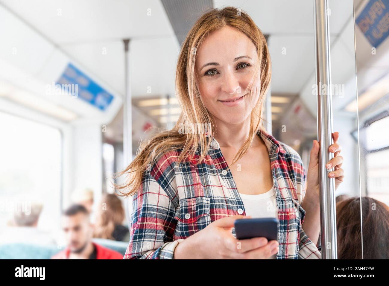 Ritratto di donna sorridente con lo smartphone sulla metropolitana di Berlino, Germania Foto Stock