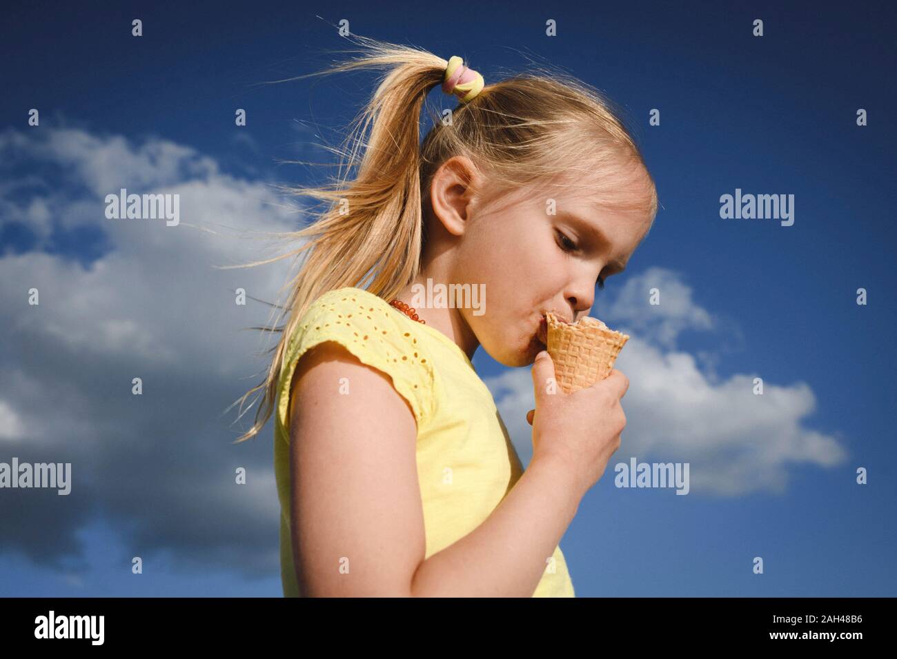 Ritratto di ragazza bionda a mangiare il gelato contro sky Foto Stock