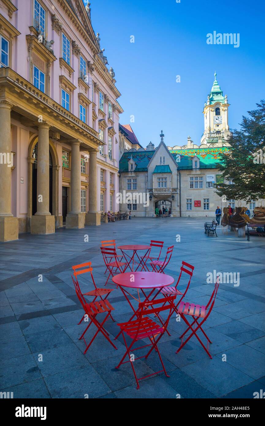 La Slovacchia, Bratislava, primati Square, Esterno del vecchio municipio rosso con tavolo e sedie in primo piano Foto Stock