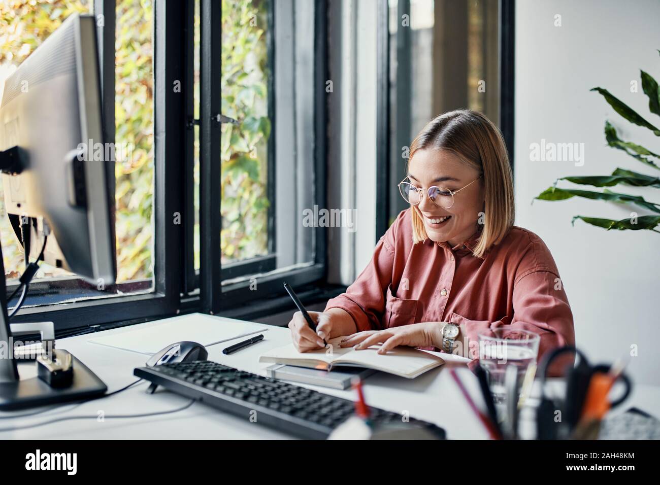 Sorridente imprenditrice prendendo appunti alla scrivania in ufficio Foto Stock