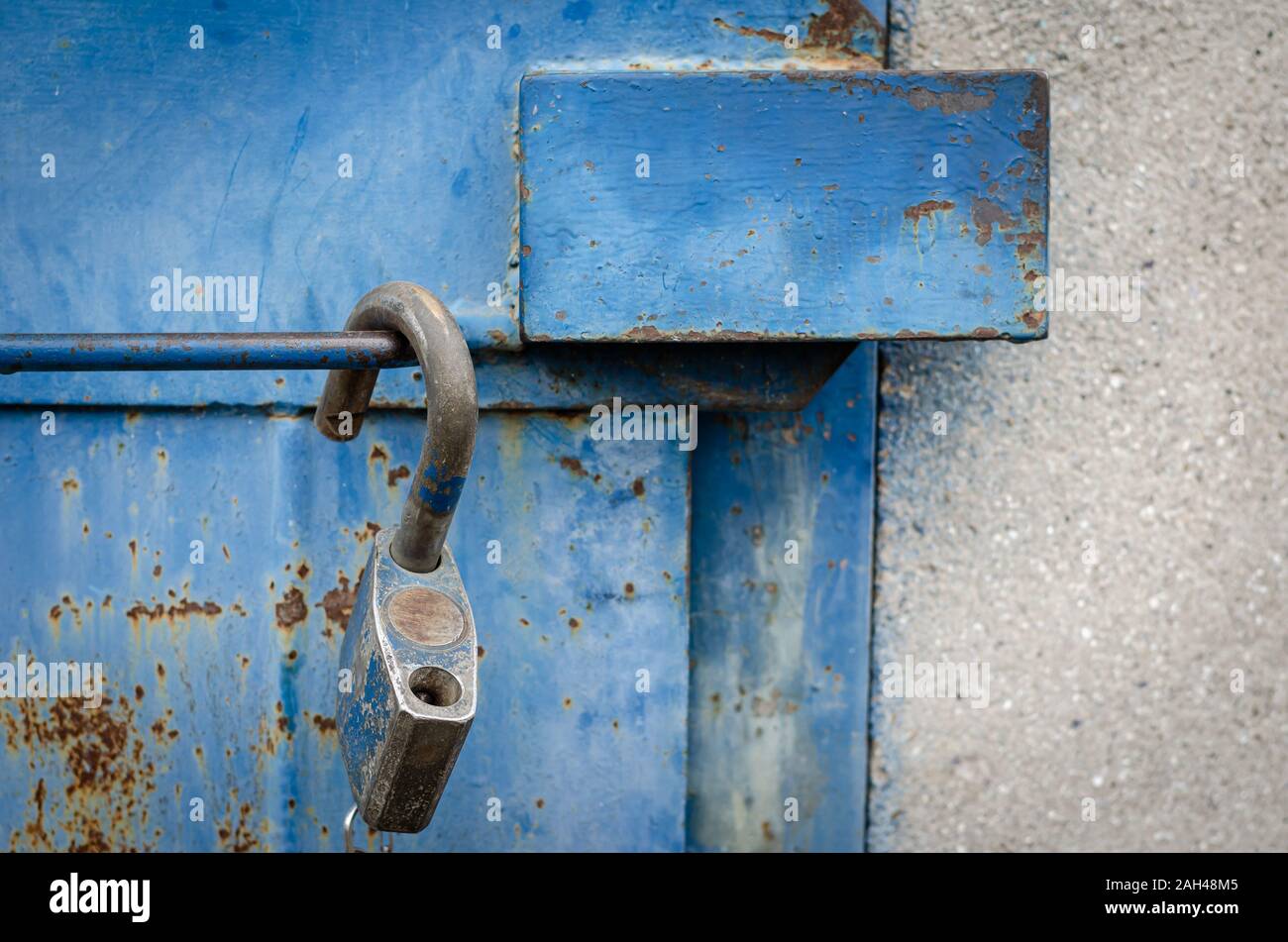Close-up di una vecchia porta di metallo con anti-vandalo protezione contro i furti. Un lucchetto aperto viene appeso sulla maniglia della porta. Il livello degli occhi di ripresa. Foto Stock