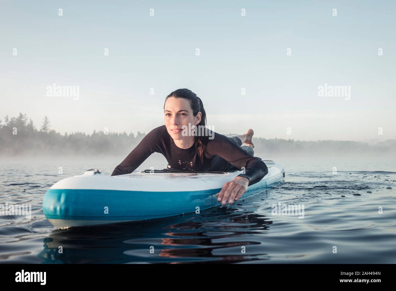 Donna sdraiata sul sup gonfiabile paddleboard sul lago Kirchsee, Bad Toelz, Baviera, Germania Foto Stock