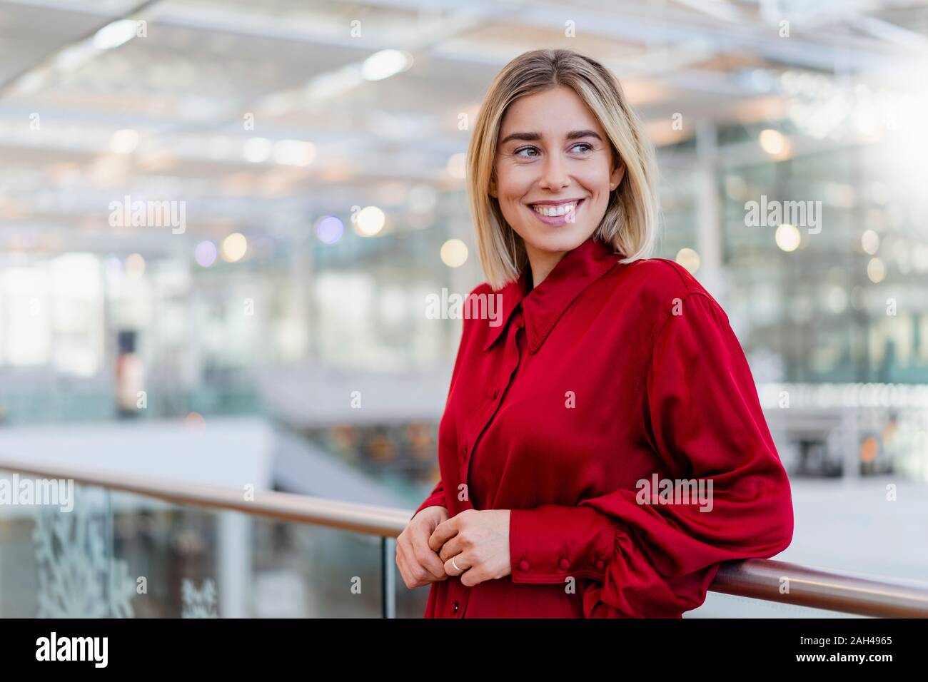 Sorridente giovane imprenditrice sta in piedi in una ringhiera guardando intorno Foto Stock