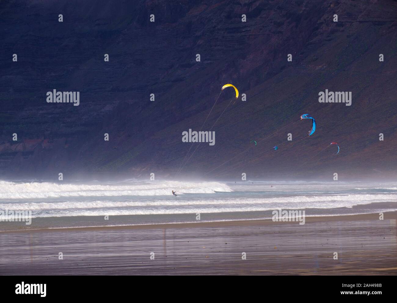 Spagna Isole Canarie Caleta de Famara, Kiteboarders a Playa de Famara con alta rupe in background Foto Stock
