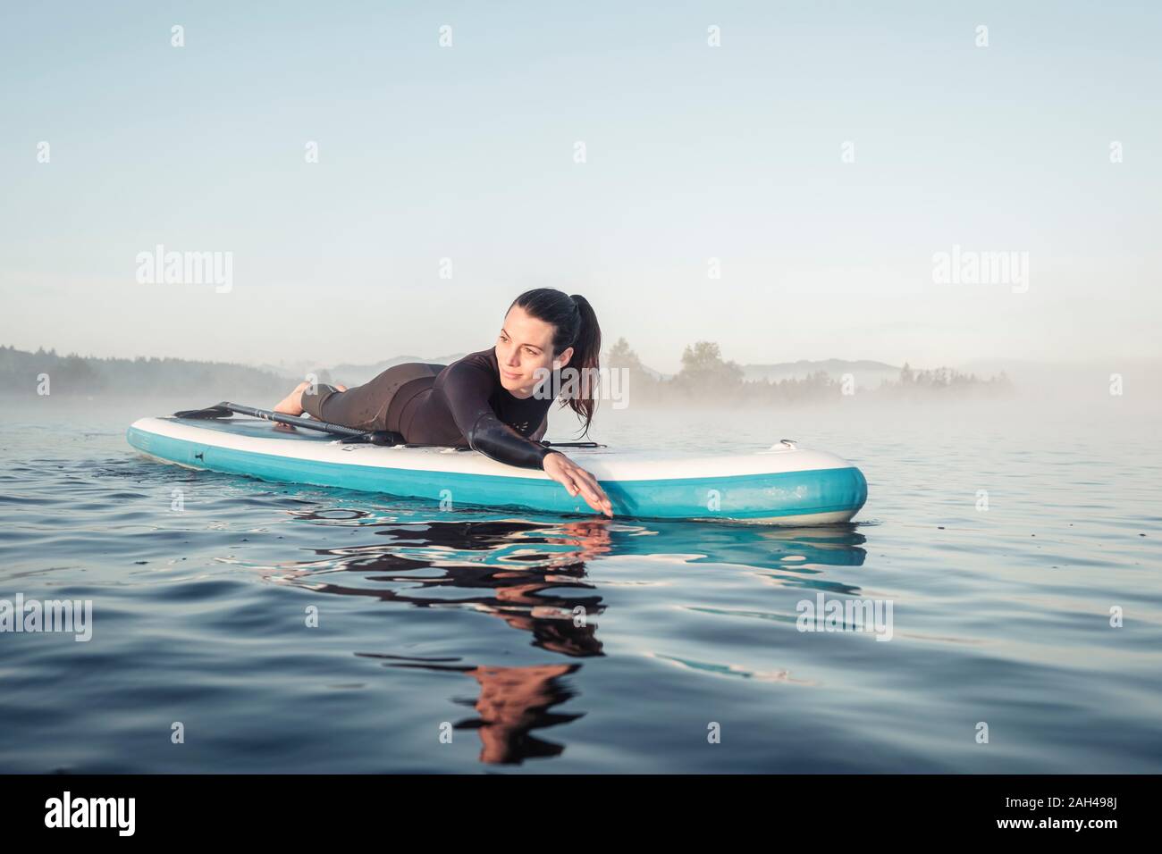 Donna sdraiata sul sup gonfiabile paddleboard sul lago Kirchsee, Bad Toelz, Baviera, Germania Foto Stock